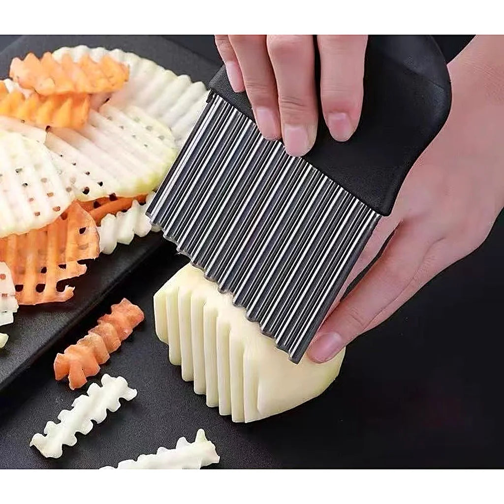 Hand using the Ovenora crinkle cutter to slice a potato, with waffle-cut vegetables on a tray beside it