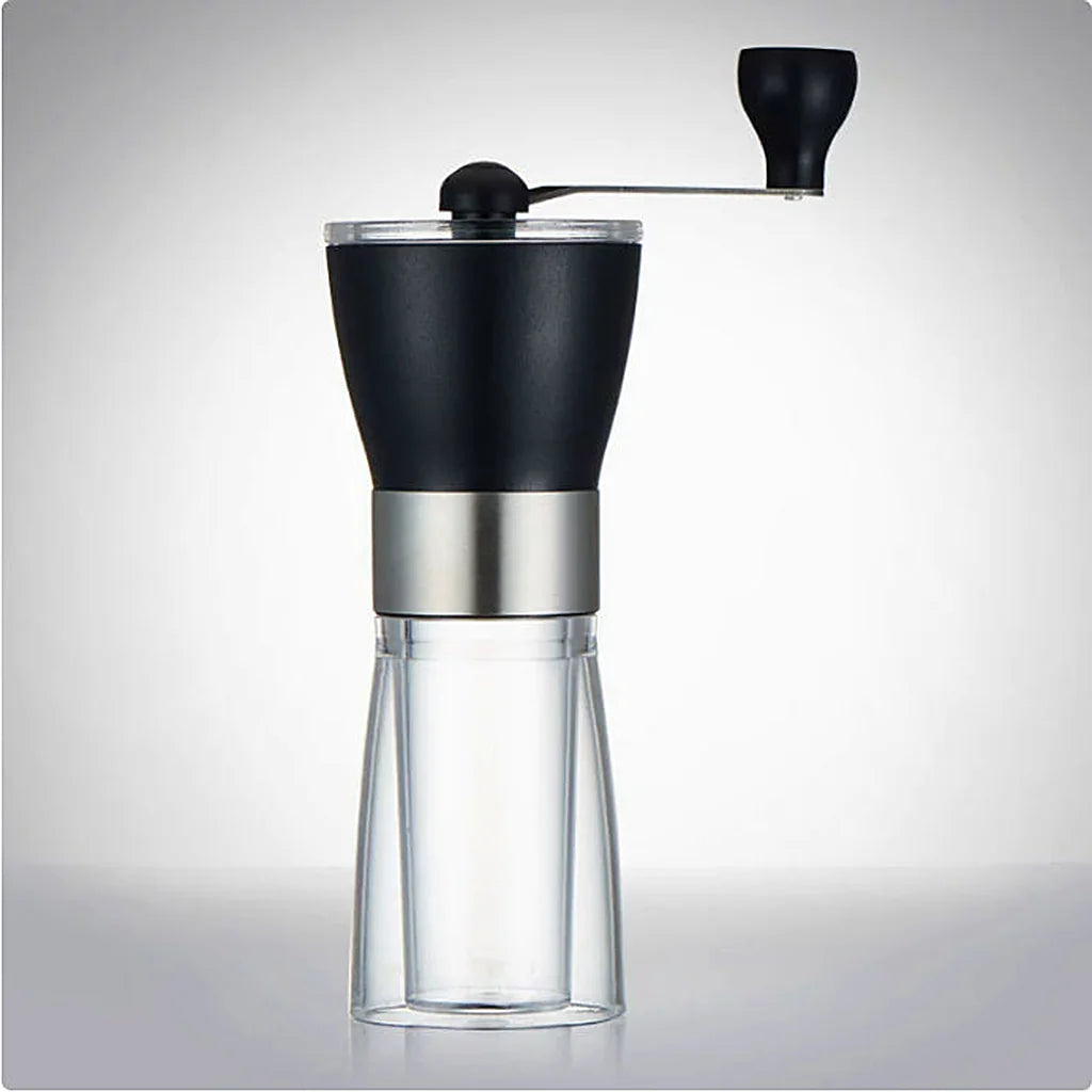Black manual coffee grinder with top crank handle, stainless steel band and clear glass grounds jar on a light background