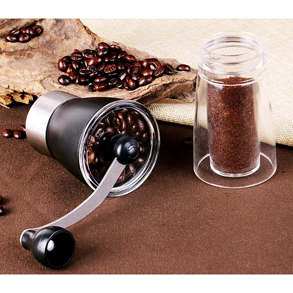 Manual coffee grinder lying on its side filled with coffee beans, clear jar of ground coffee beside it on burlap