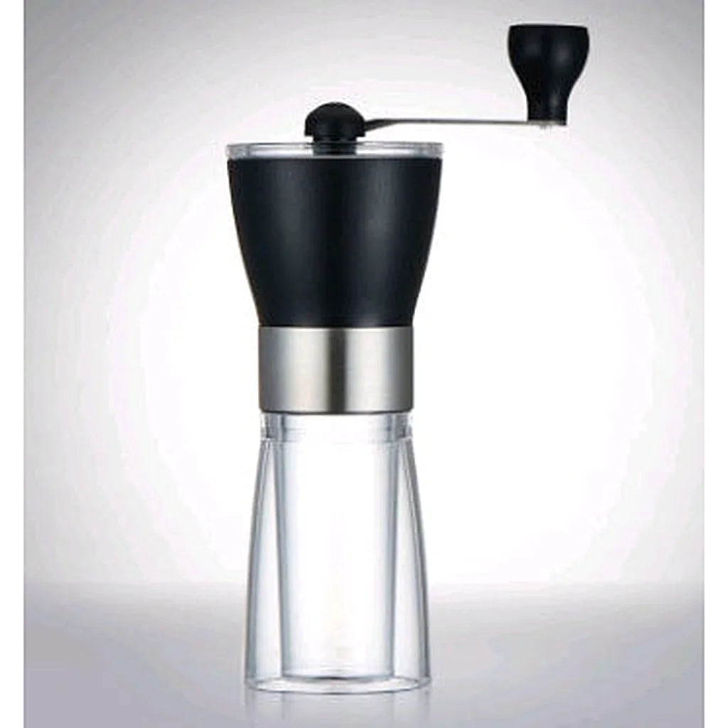Assembled black hand-crank coffee grinder with clear glass collection jar against a soft grey studio background