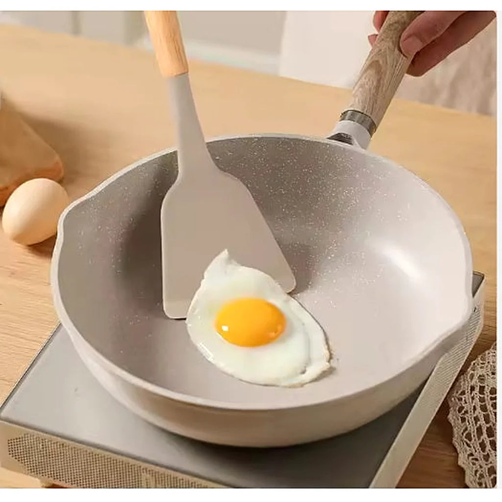 Khaki silicone turner sliding under a fried egg in a light-colored frying pan on a stovetop