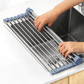 Hands unrolling the stainless steel roll-up dish rack with blue silicone edges across a kitchen sink