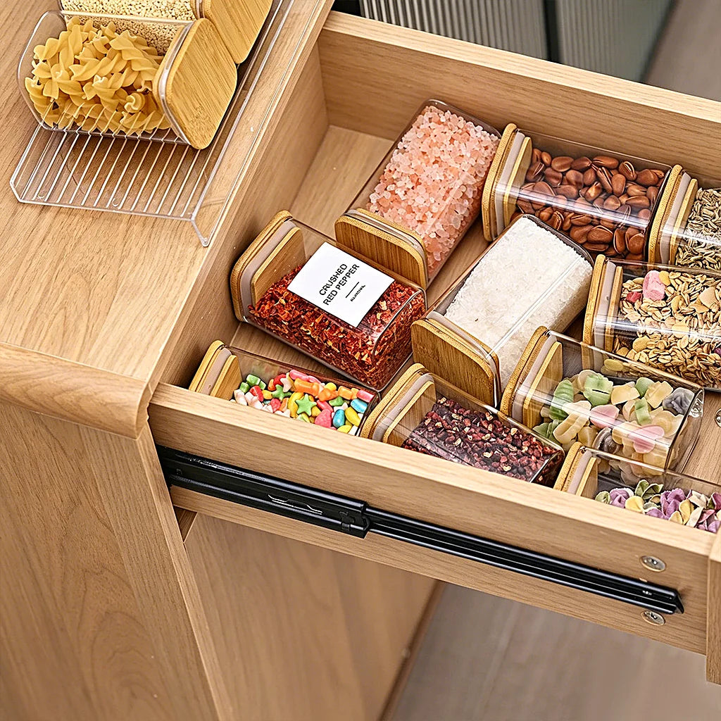 Open wooden kitchen drawer with clear spice jars lying flat inside, and the clear rack on the counter beside it
