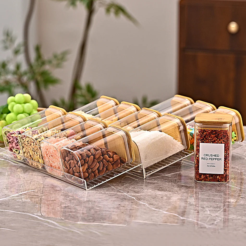 Two tiered spice racks side by side on a reflective marble counter with grapes and a plant in the background