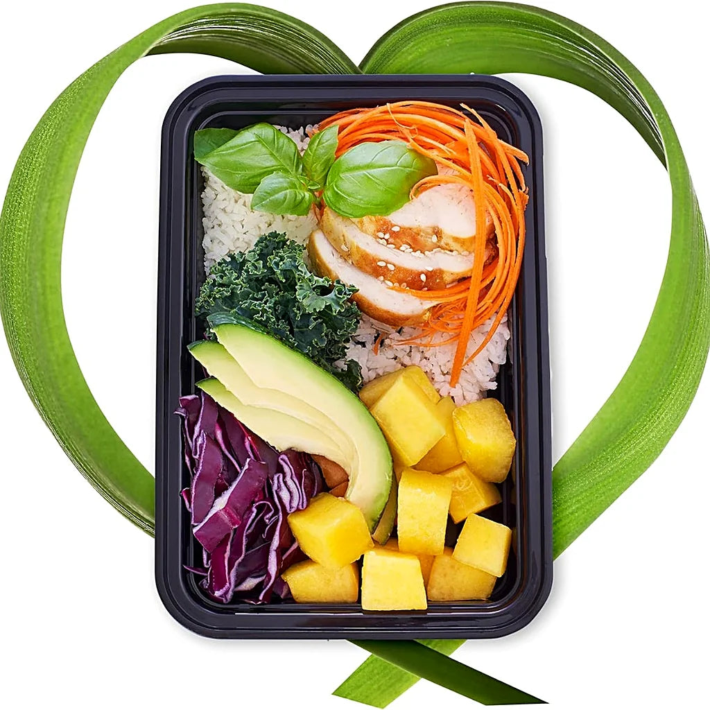 Meal prep container filled with rice, sliced chicken, avocado, mango, red cabbage and kale, framed by curved green leaves
