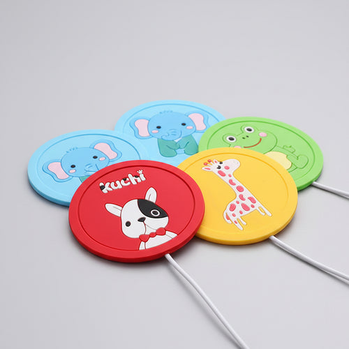 Two round silicone coasters with cartoon designs on a wooden surface.
