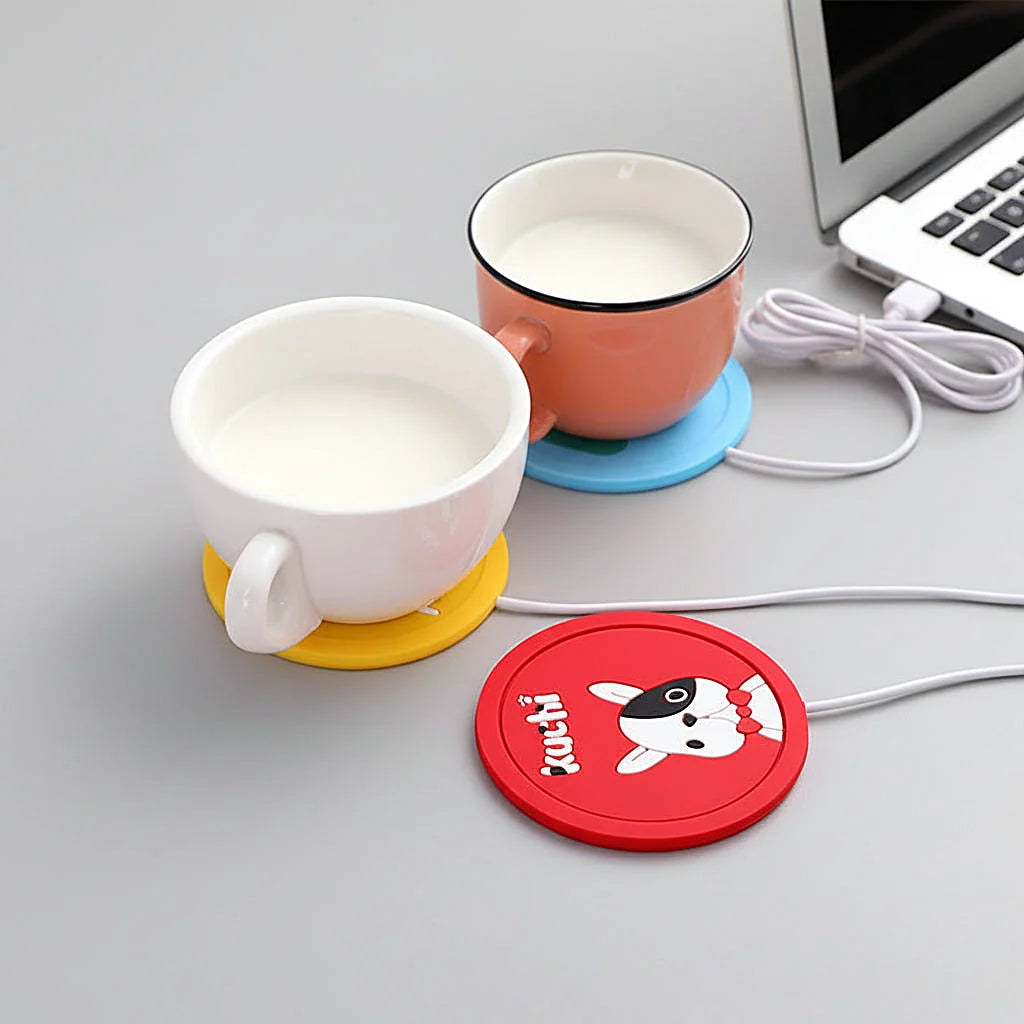 Two cups of milk on yellow and blue warmer pads beside a laptop, with a red dog-design pad in front