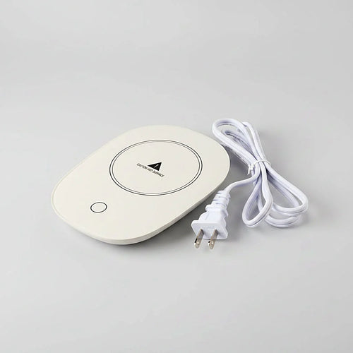 White oval mug warmer pad beside its power cord with a US plug on a light gray background